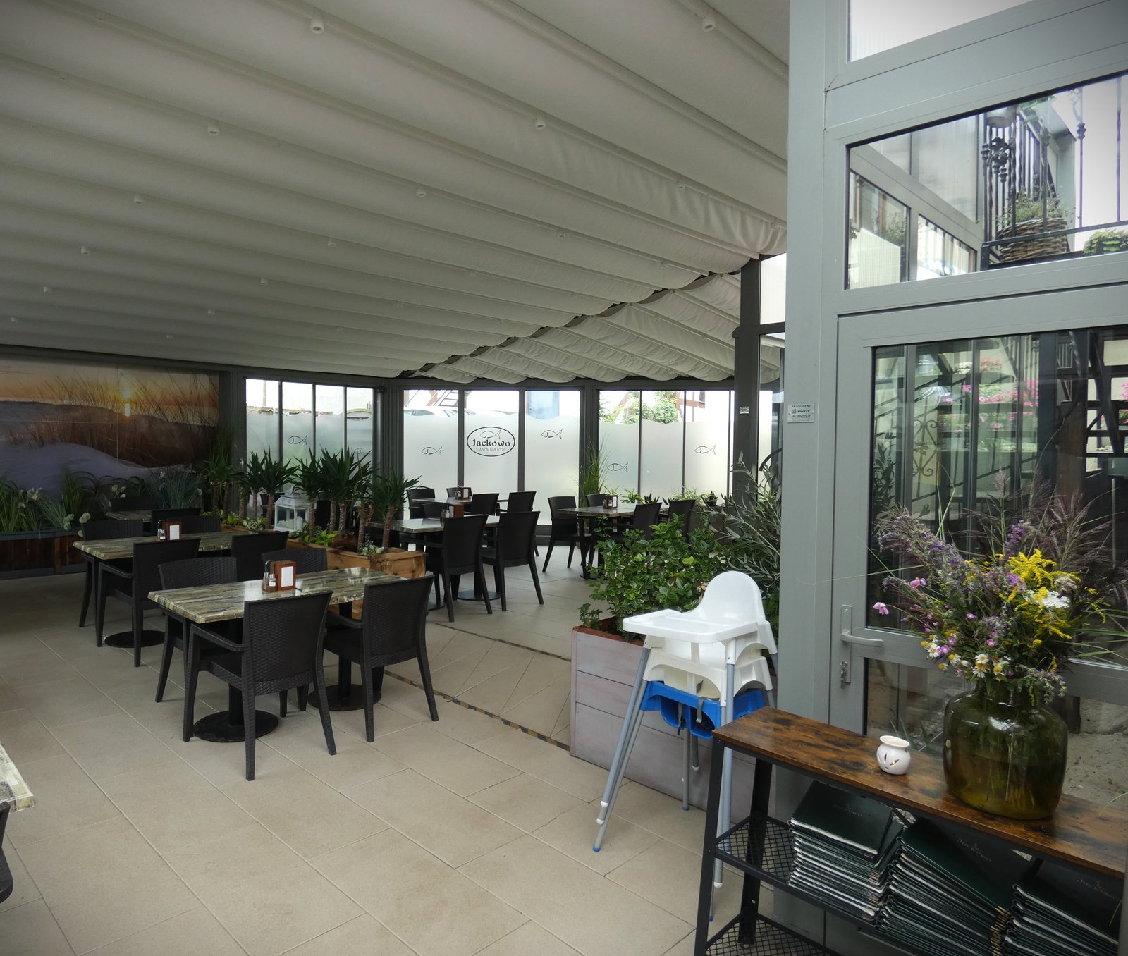 Zadaszony taras restauracji z fototapetą wydm i stolikami